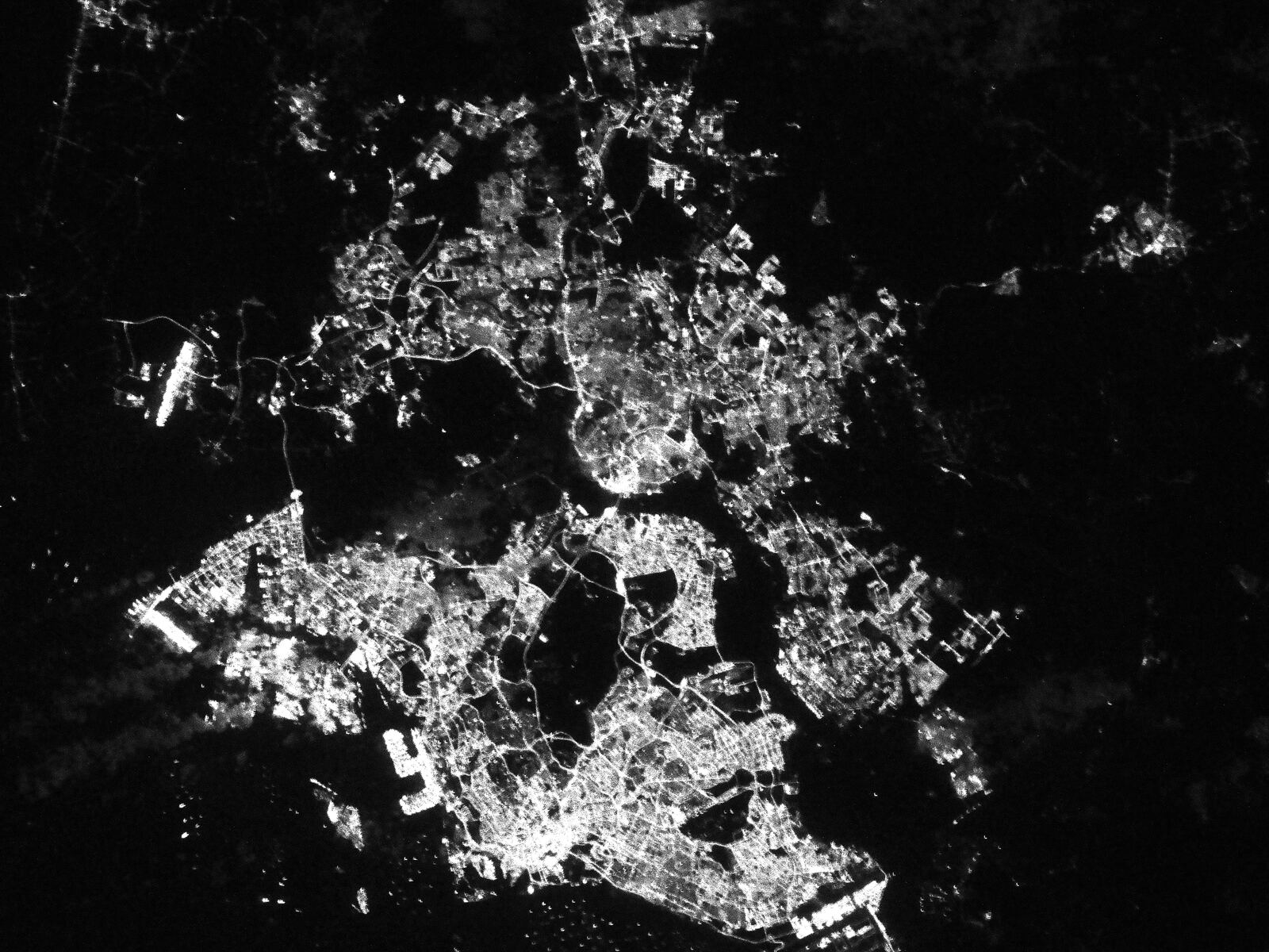 Singapore and southern Johor at night, photographed from the International Space Station. The two cities read as a white lattice of streets and the strait between the two countries is dark, with the anchorage off the island scattered with points of light.